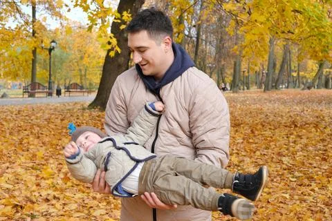 Father picking up son while standing in autumn park Stockfoto's