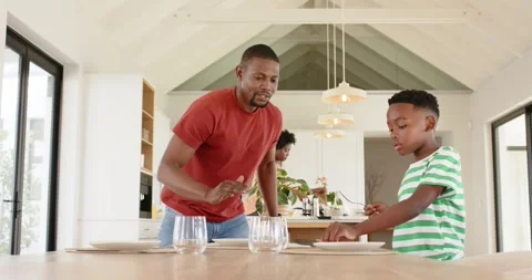 Father placing square plate, guiding son aligning on table for meal in kitchen Stock Footage 342595760