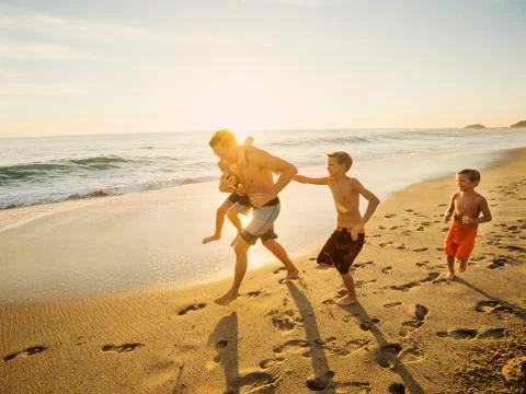Father playing football on beach with his three sons (6-7, 10-11, 14-15) Stock Photos