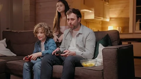 Father playing with his son in game console and winning, sitting on sofa Stockbeeldmateriaal 165415744