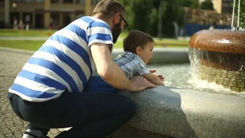 Father playing with his son next to the fountain in the park Stock Footage 76980068