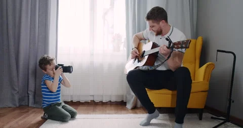 A father plays guitar while his son captures the moment, bonding Stock Footage 307299594