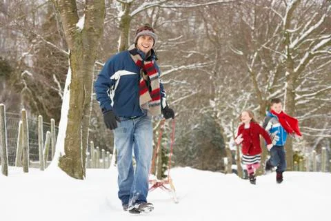 Father pulling children on sledge through winter landscape Foto stock