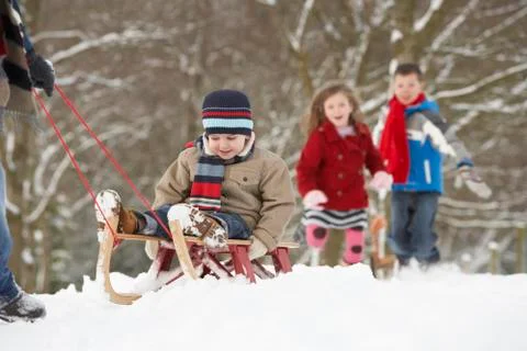 Father pulling children on sledge through winter landscape Stock Photos