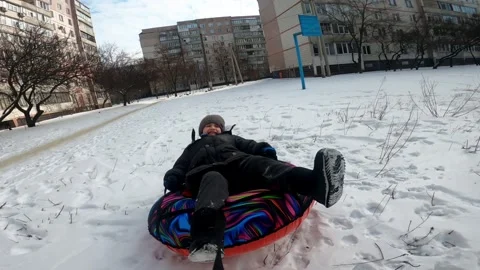 Father pulling his six year old son on an inflatable snow ride in winter Stock Footage 326793653