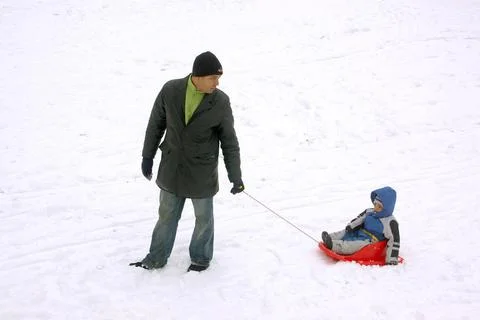Father pulling son sitting on red coloured Pulka in winter ; Gothenburg ; ... Foto stock
