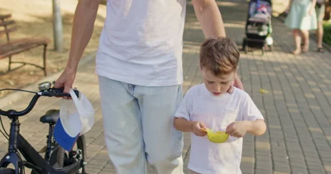Father pushes bicycle while son walks beside eating ice cream Stockbeeldmateriaal 316761959