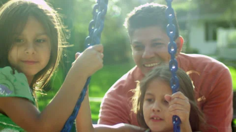 Father pushes his two daughters on a tire swing in a park. Stock Footage 33871337