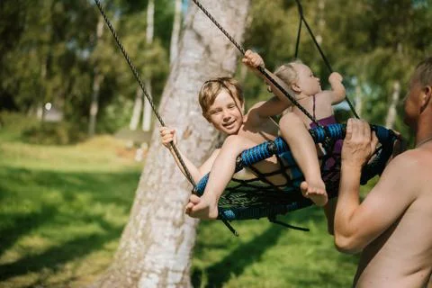 Father pushing children sitting on swing at playground. Summer in the nature. Stock-Fotos