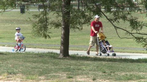 Father pushing stroller while son rides bicycle (2 of 2) Stock Footage 32027511