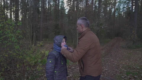 Father puts scarf on top of jacket for son among forest Stock Footage 241178056
