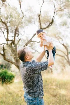 Father raises his son up in his arms and holds him above in the olive grove Stock Photos