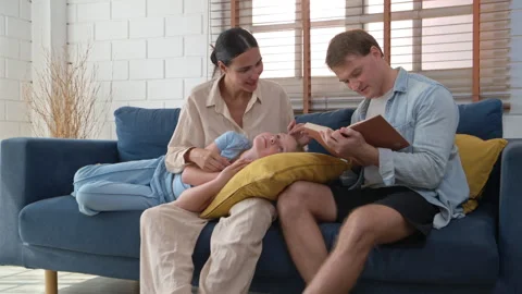 Father reading book while daughter resting on mother lap Stock Footage 340144438