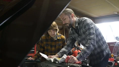 Father referencing car instruction manual, teenage son watching. Stock Footage