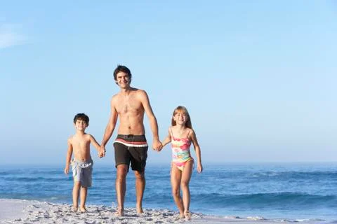 Father Running With Children Along Sandy Beach Stock Photos