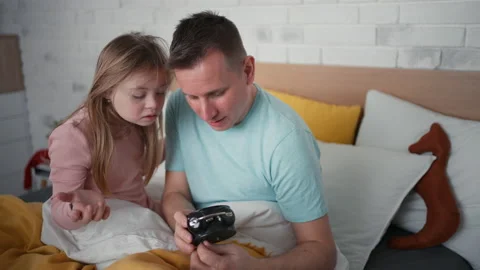 Father setting alarm clock with his little daughter with Down syndrome in bed at Stock Footage 171595864