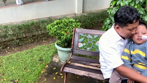 Father Sitting on Park Bench Supporting Child with Special Needs Stock Footage 328634627