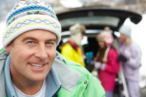 Father Smiling At Camera Whilst Family Load Skis In Boot Of Car Stock Photos