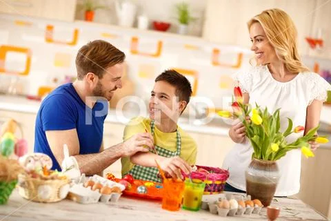 Father with son painting eggs while mother arranges tulips Stock Photos