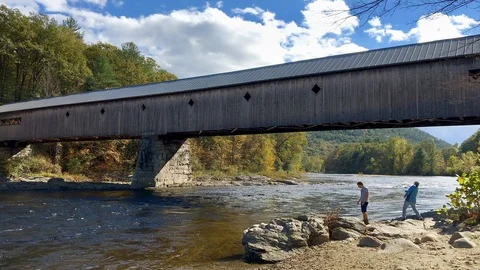 Father &amp; Son Skipping Rocks on River under Covered Bridge in New England Stock Footage 98416136