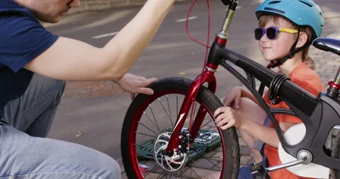Father with son squats down working together to fix bicycle Video stock 285496894