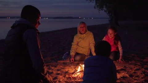 Father stroking son on head by campfire during family hike on beach Stock Footage 108434888