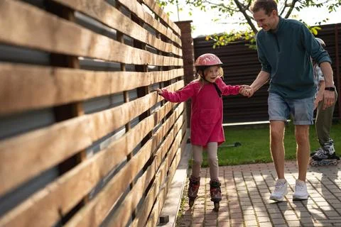 Father Supporting Daughter Learning Roller Skating Outdoors Photos
