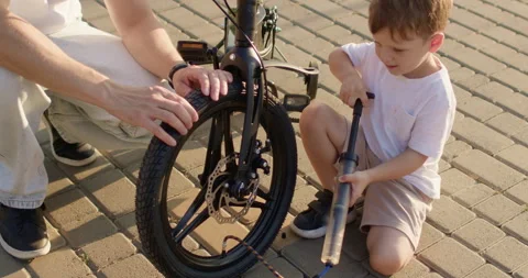 Father supports bicycle while smiling boy holds hand pump 動画素材 316763653