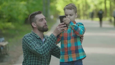 The father teaches his son how to use the phone and teaches him to take selfi Stock Footage 147282974