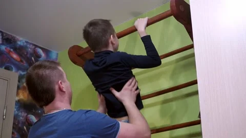 The father teaches his son to pull up on the horizontal bar at home. playing Stock Footage 170447549