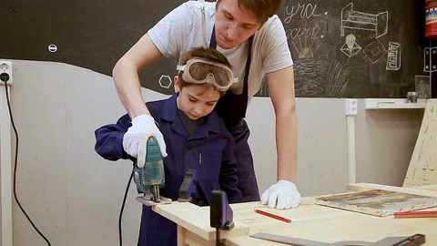 The father teaches his son to work with an electric jigsaw  on wood Stock Footage 102239888