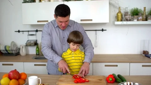 Father teaching his son to chop vegetables in the kitchen at home. Cut pepper Stock Footage 83428814
