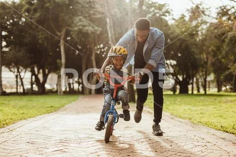 Father teaching his son cycling at park Stock Photos
