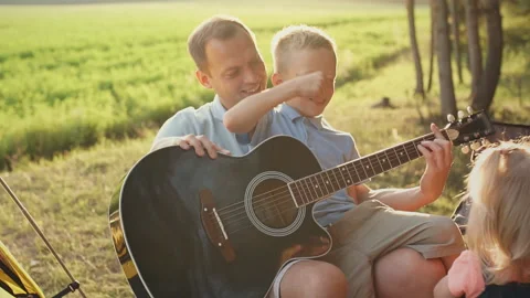 Father teaching his son how to play the guitar in outdoor. Slow motion Stock Footage 124090787
