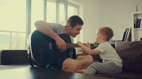Father teaching his son to play on guitar at home. Video stock 80217495