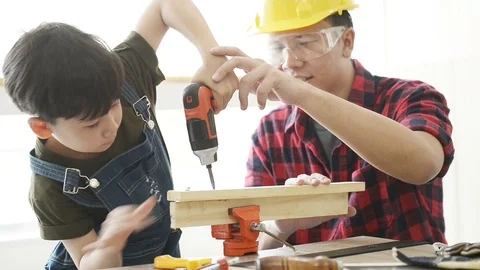 Father teaching his son use left hand electric drill for fasten the wood plank. Stock Footage 114873717