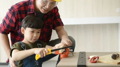 Father teaching little son using manual wood saw for sawing wood sheet. Vidéo 114675061
