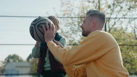 Father teaching son how to hold and throw a basketball ball on a court 스톡 동영상 166837027