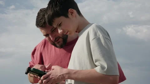 Father Teaching Son How to Operate a Drone with a Remote Controller Outdoors Stock Footage 335768652