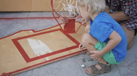 Father teaching son how to screw bolt into wooden basketball board Stock Footage 61477141