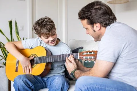 Father teaching son playing guitar at home Stock Photos