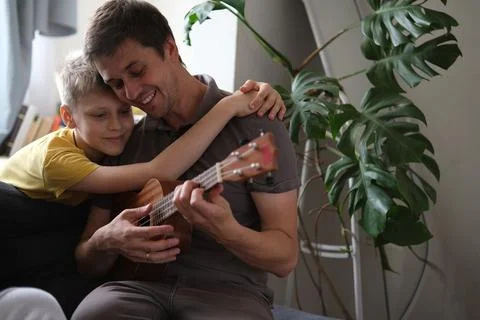 Father teaching son ukulele, smiling and bonding warmly at home Stock Photos