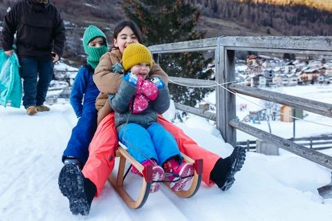 Father with three daughters going down on snow slope with wooden sled 스톡 사진