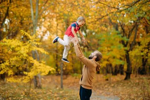 Father throws his son up while walking in the autumn forest. Stock Photos