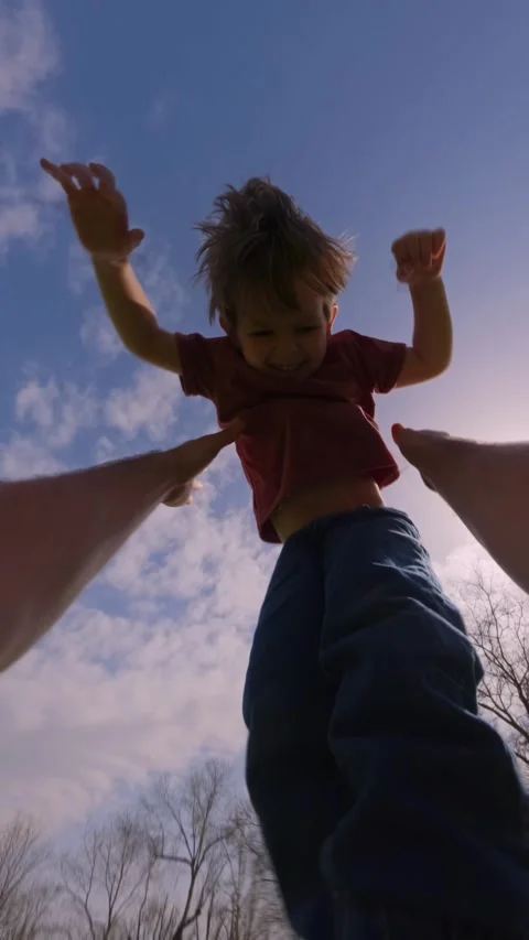 Father tossing his laughing son into the air against a bright sky in a park Stock Footage 305318924