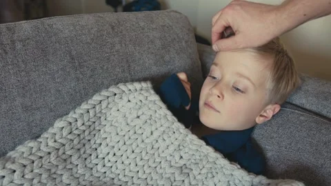 Father touching forehead of sick son resting on sofa 動画素材 346969596