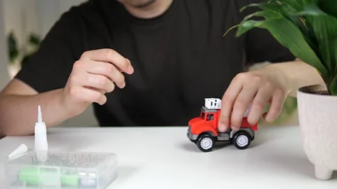 A father with a toy car whose wheels are broken tries to put them back on but Stock Footage 313866633