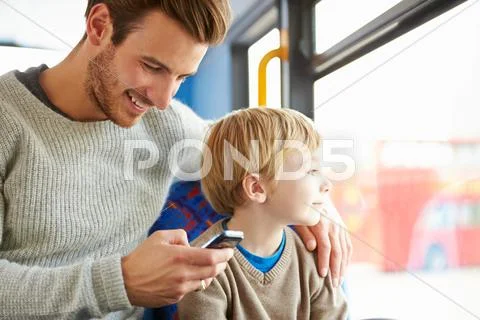 Father using mobile phone on bus journey with son Stock Photos