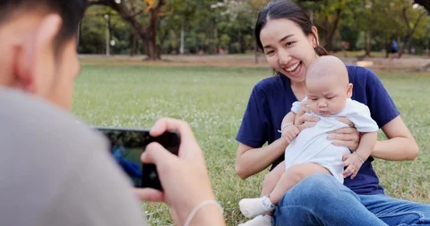 Father using smartphone to taking photo with his wife and baby at park. Stock Footage 106750203