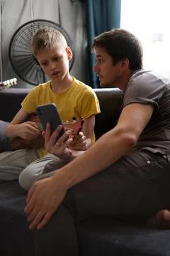 Father using smartphone teaching son to play ukulele at home Stock Photos